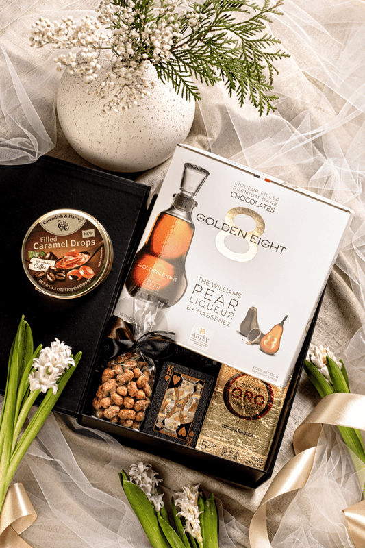 Elegancki męski zestaw prezentowy w otwartym czarnym pudełku z kawą Lavazza, pralinami Abtey i czarnymi kartami do gry.