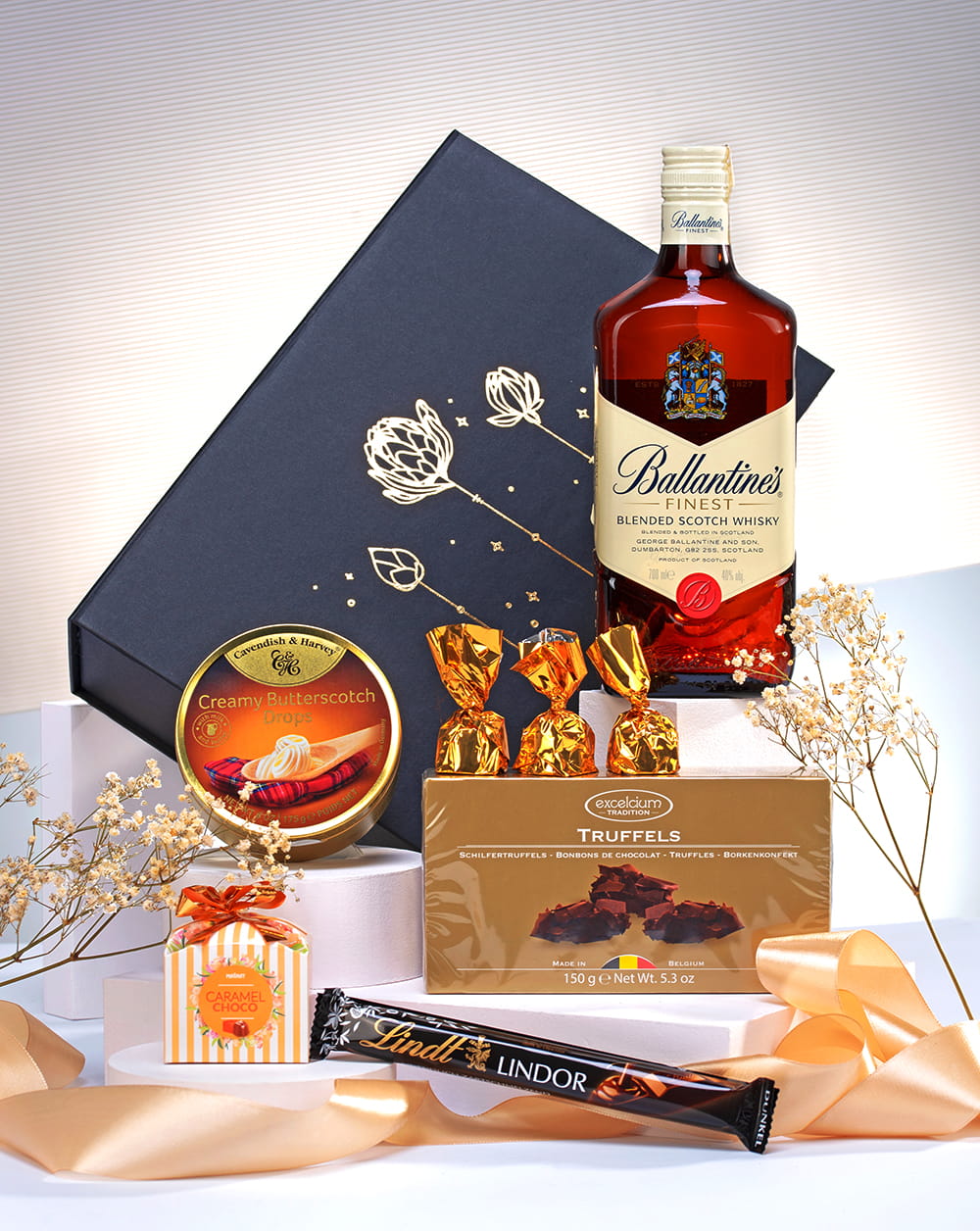 Elegancki kosz prezentowy z whisky Ballantines Finest, czekoladą Lindt, truflami i pralinami w czarnym pudełku ze wstążką.