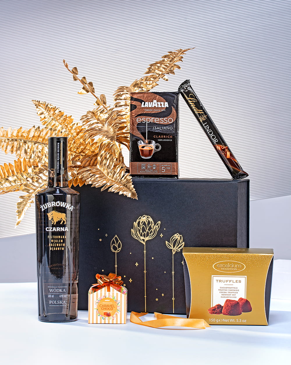 Luksusowy zestaw prezentowy dla mężczyzny w otwartym czarnym pudełku z wódką Czarna Żubrówka, kawą Lavazza i pralinami.