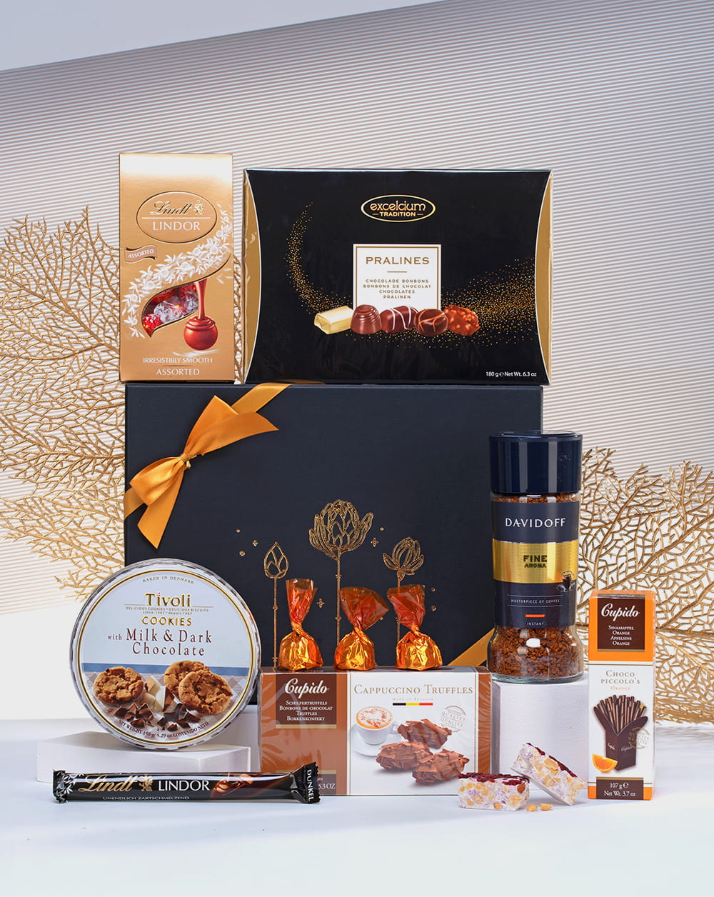 Elegancki zestaw prezentowy w otwartym czarnym pudełku ze złotymi detalami, z kawą Davidoff, pralinami Lindt i czekoladkami.