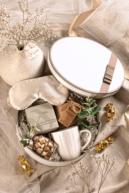 Otwarty, okrągły kremowy zestaw prezentowy z herbatą, kubkiem, świecą bąbelkową, satynową opaską i karmelkami. Idealny prezent na imieniny i relaks.
