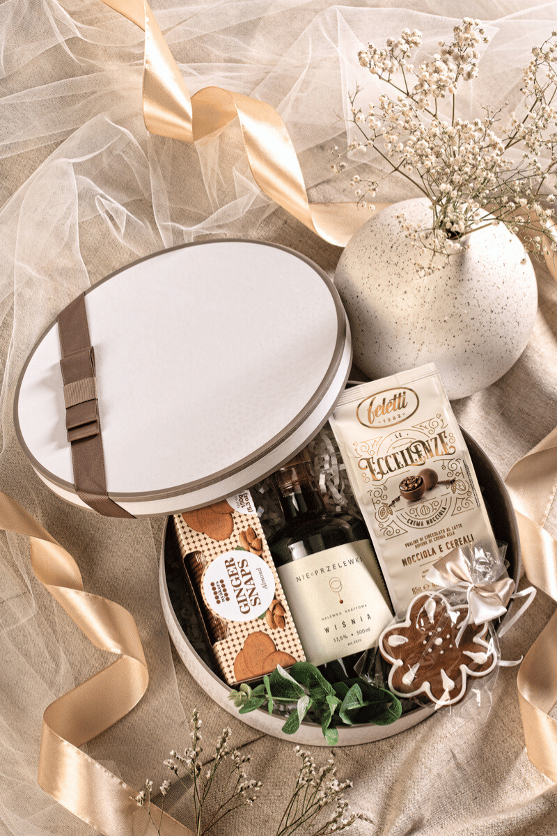 Elegancki zestaw prezentowy dla kobiety z kraftową nalewką wiśniową, pralinami i piernikiem, w kremowym pudełku z beżową kokardą.