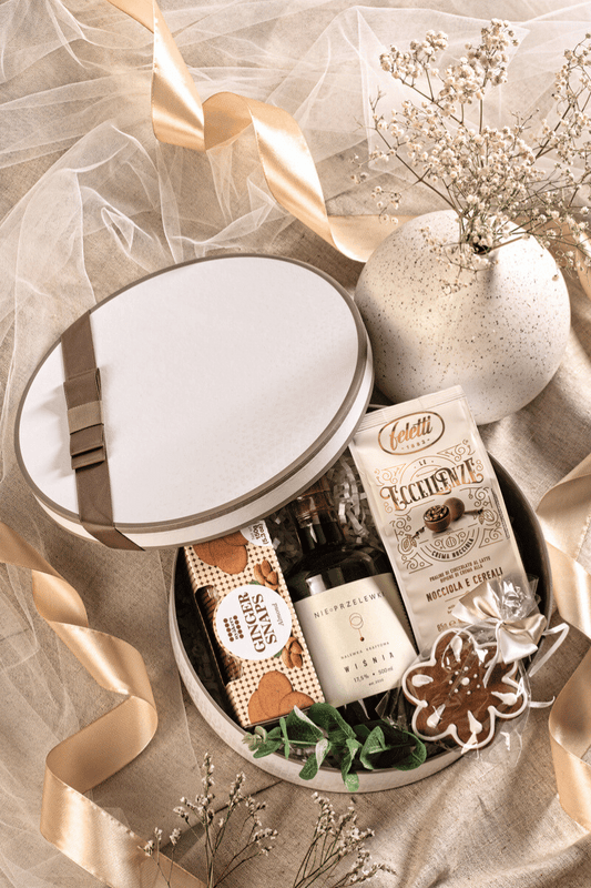 Elegancki zestaw prezentowy dla kobiety z kraftową nalewką wiśniową, pralinami i piernikiem, w kremowym pudełku z beżową kokardą.
