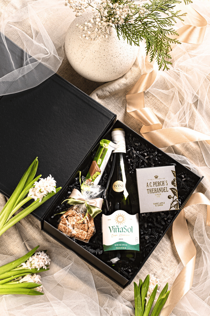 Elegancki zestaw prezentowy w otwartym czarnym pudełku z winem Vina Sol Torres, pistacjową czekoladą i herbatą.