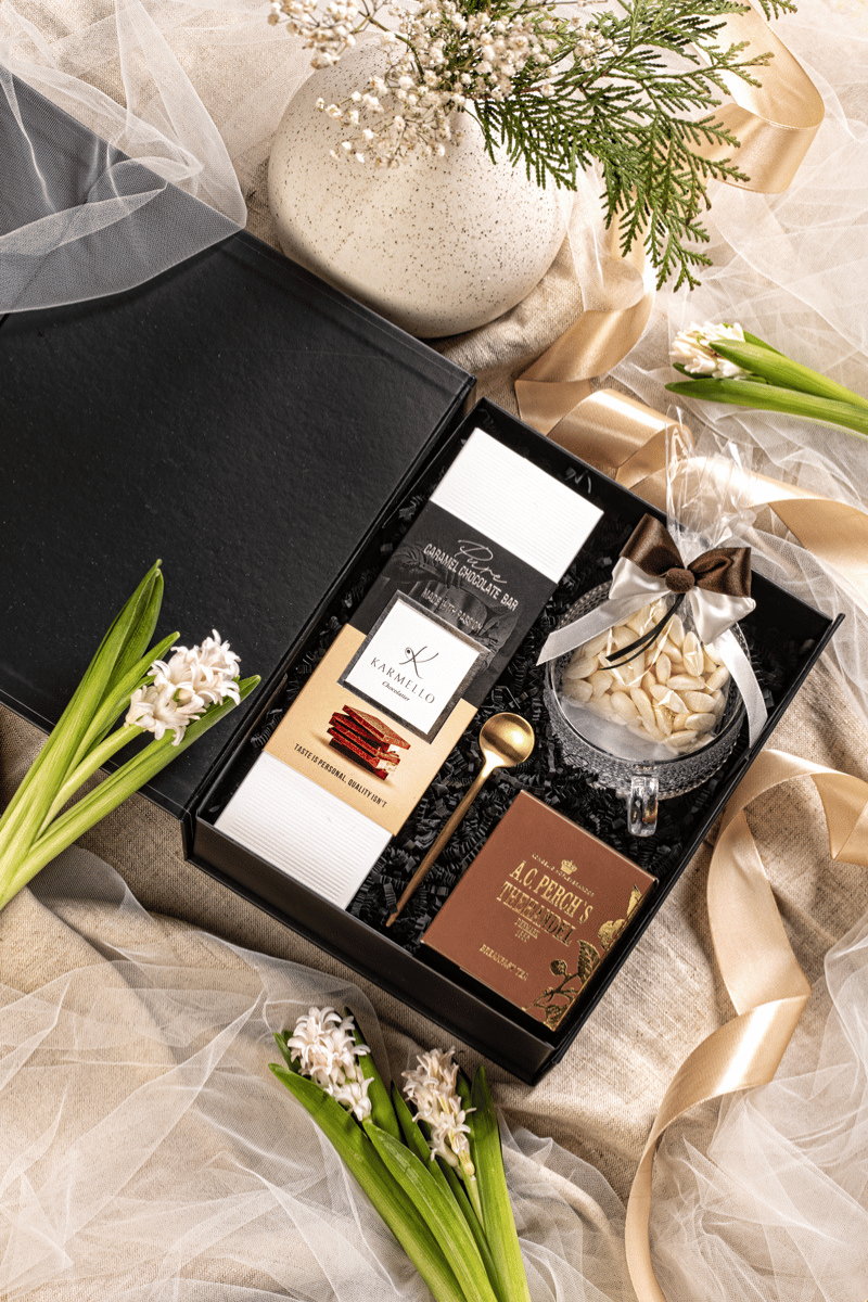 Ekskluzywny zestaw herbaciany w eleganckim czarnym pudełku, z filiżanką, herbatą A.C. Perch's, czekoladą Karmello i migdałowymi karmelkami.