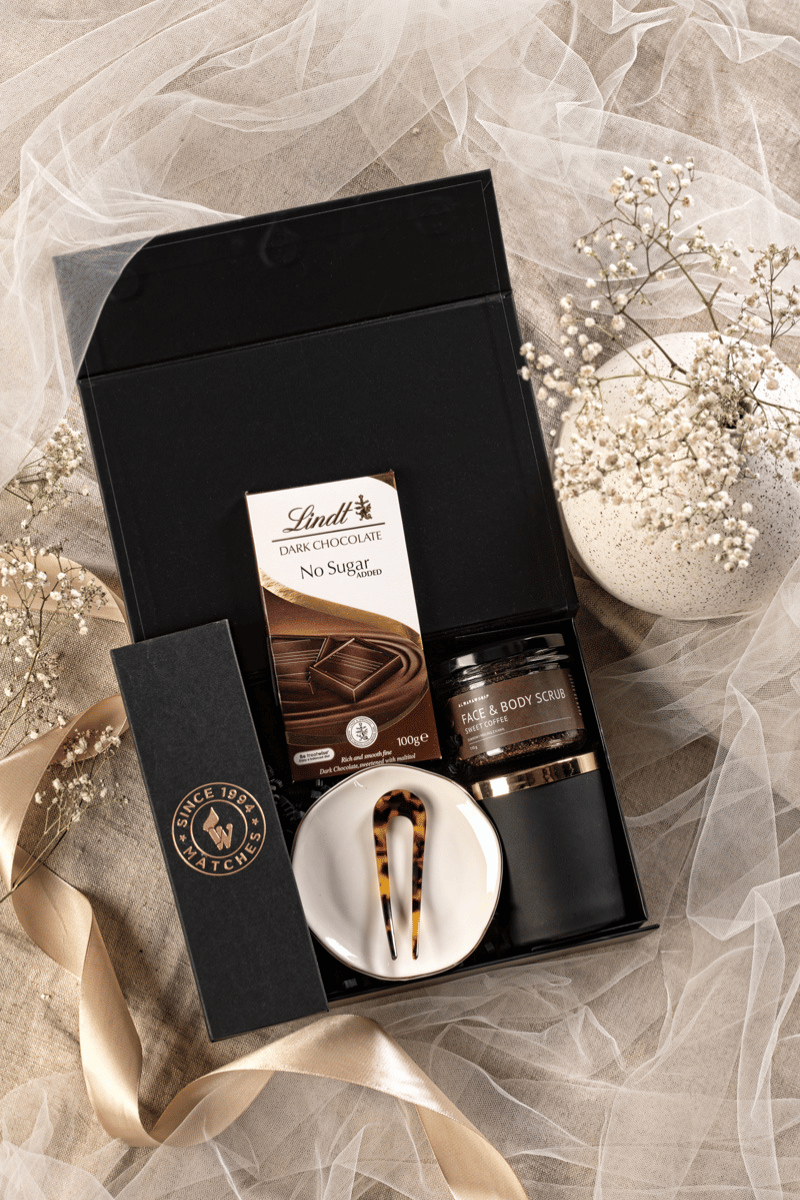 Luksusowy zestaw prezentowy dla kobiety w otwartym czarnym pudełku z kawowym peelingiem, świecą sojową i podstawką.