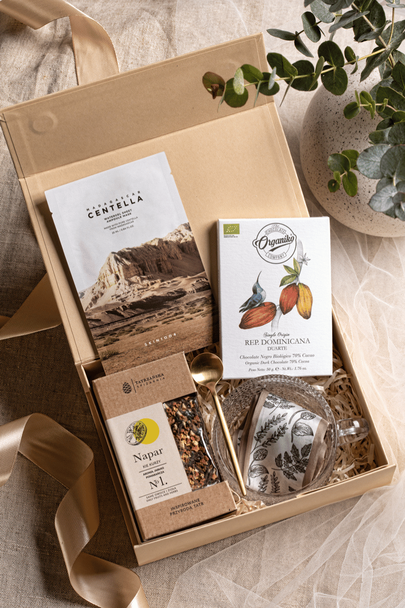 Beżowe pudełko prezentowe Maryna z satynową kokardą, z zestawem relaksacyjnym dla kobiety: maską SKIN1004, naparem i filiżanką.