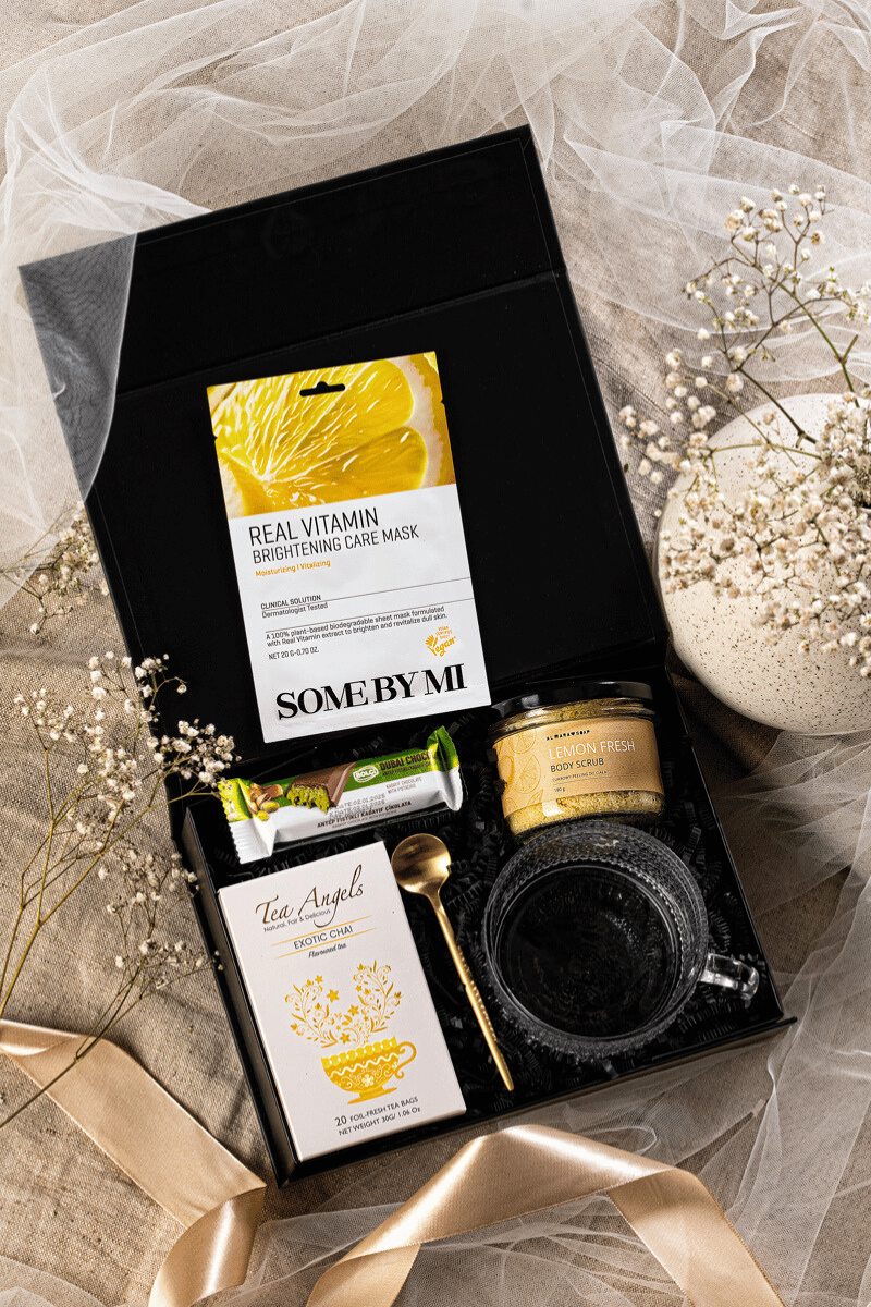 Elegancki zestaw prezentowy SPA w czarnym pudełku z kokardą, zawierający cytrynowy peeling, maseczkę, szklaną filiżankę i herbatę.