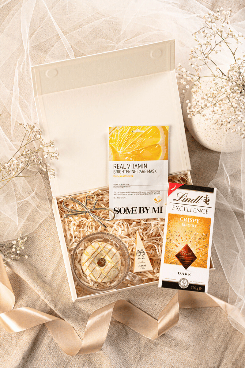 Zestaw podarunkowy dla kobiety w beżowym pudełku, z elegancką filiżanką, herbatą Charbrew, mydełkiem pistacjowym i czekoladą Lindt.