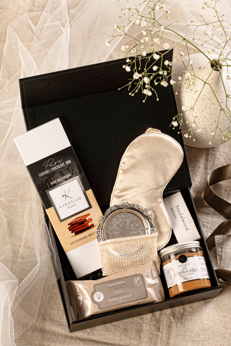 Luksusowy zestaw prezentowy dla kobiety w czarnym pudełku: satynowa opaska, kosmetyki Rituals i słodycze Karmello.