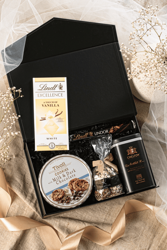 Elegancki zestaw prezentowy w białym pudełku z kokardą: herbata Chelton, praliny Karmello i czekolady Lindt.